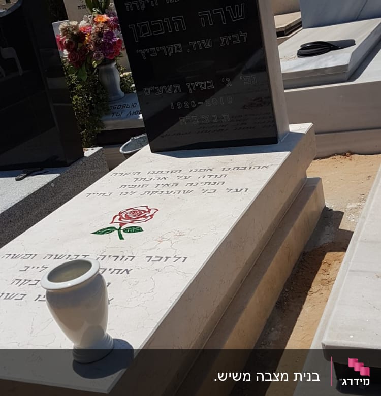 מצבות עם כיתוב בעברית ופרחים על קבר